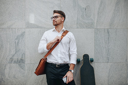 Businessman standing against a wall with a longboard