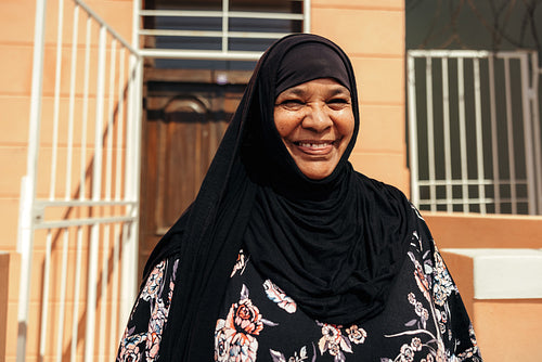 Happy Muslim woman smiling at the camera outside her home