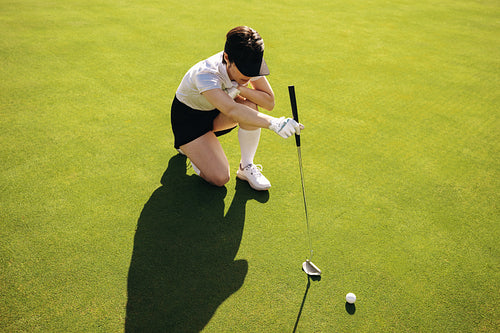 Close shot of woman golfer crouching and aiming a putt on the green of an immaculate course