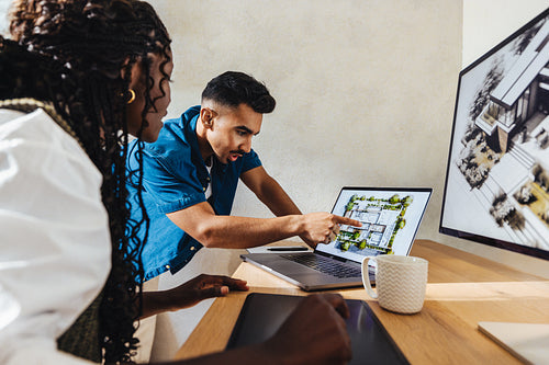Two architects discussing a residential project while reviewing architectural plans on a laptop
