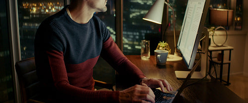 Man working on laptop late at night in office overlooking city