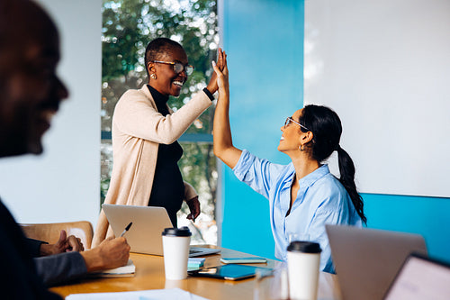 Two women celebrating success with high five in an office meeting
