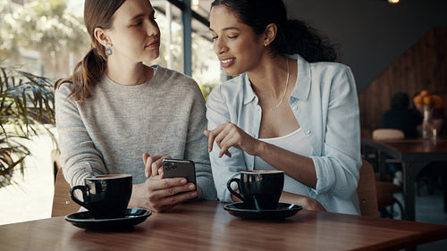 Friends at a cafe using a mobile phone and smiling