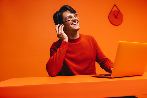 Happy salesman in vibrant orange workspace using laptop and headset, emphasizing creative and modern sales environment