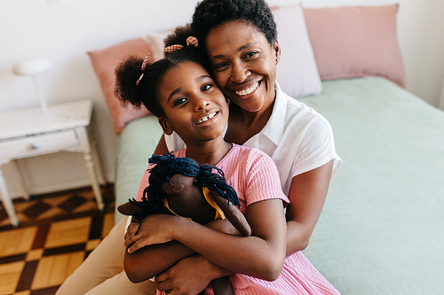 Mom sitting on the bed, cuddling her daughter and her doll
