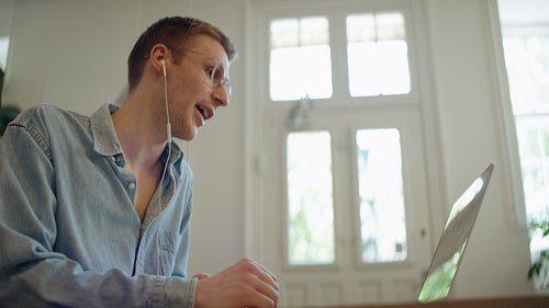 Laughing man talks on a laptop for an online meeting in an indoor workspace