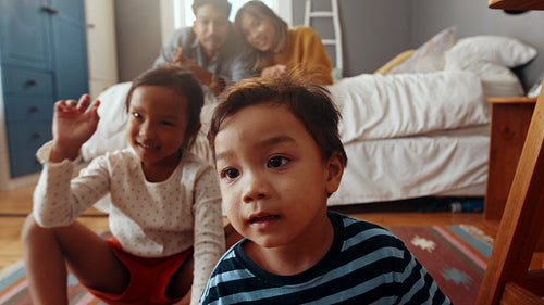 Two young siblings playing and talking directly in front of the camera in their parents’ room