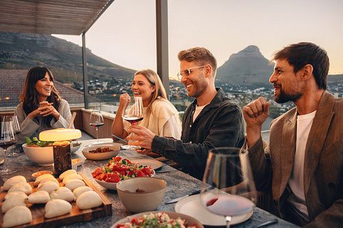 Friends enjoying an outdoor dinner party at sunset with food and drinks