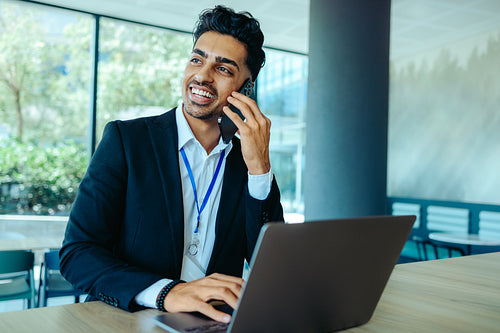 Indian businessman in corporate office using phone and laptop