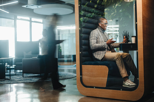 Professional businessman using a laptop for a virtual meeting in a privacy booth