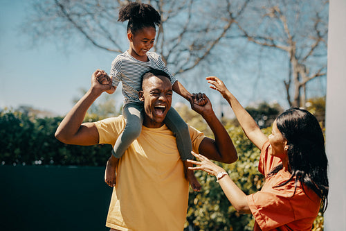 Father carrying his daughter on his shoulders while standing outside. Parents having fun with their kid
