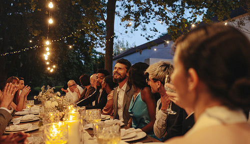 Outdoor evening wedding reception with guests dining under string lights