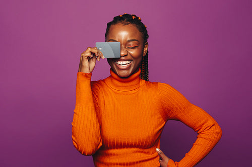 Happy woman paying with a card against a vibrant purple background