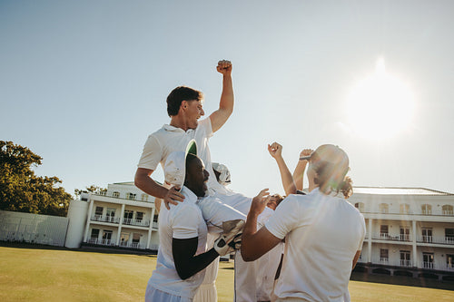 Cricket team celebrating player victory under bright sun near pavilion