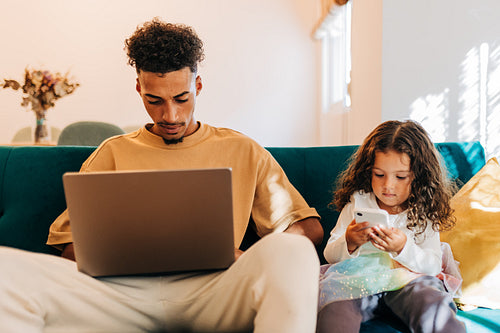 Father and daughter using their mobile devices at home