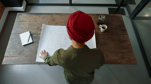 Woman in a headscarf laying out a blueprint drawing for review in an office
