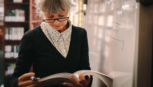 Portrait of a senior woman looking at a book in library