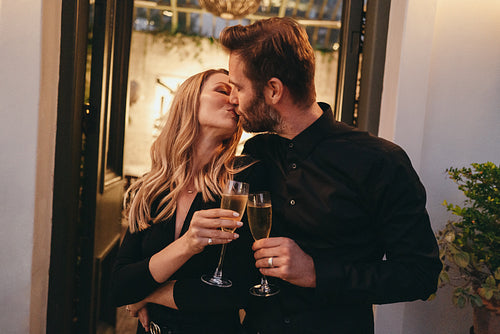 Affectionate married couple kissing while holding wineglasses