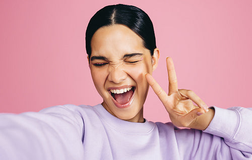 Excited woman taking a selfie and doing a peace sign in a studio