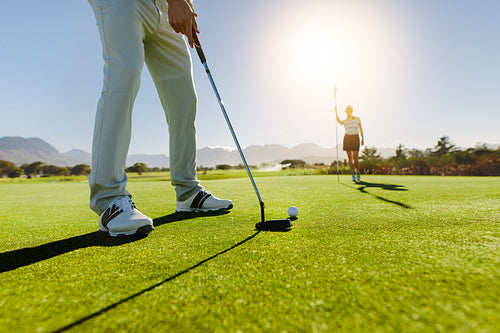 Golfer putting ball with female partner holding flag on golf course