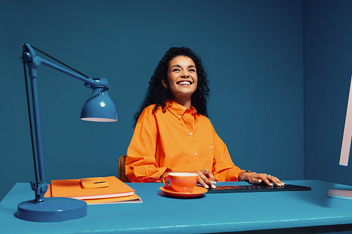 Happy worker with curly hair sitting at colorful desk