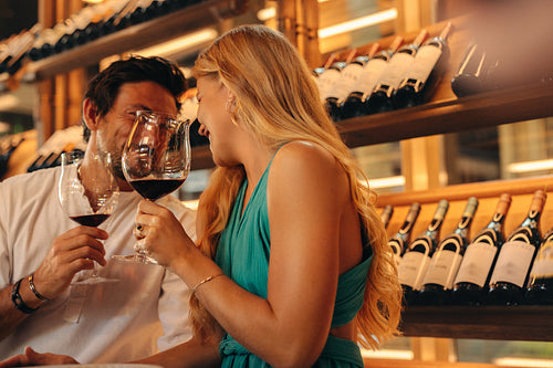 Couple talking and drinking wine in front of a wine rack with bottles in the background