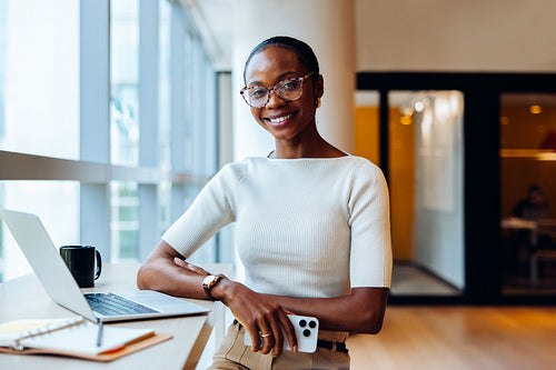 Confident young professional woman with a laptop and notepad in office