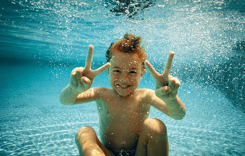 Joyful child underwater showing peace signs in a swimming pool
