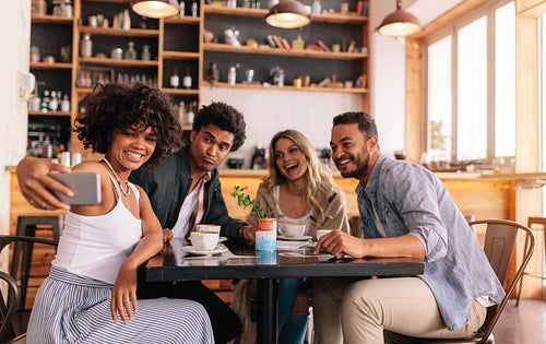 Diverse group of friends taking selfie on smart phone at cafe