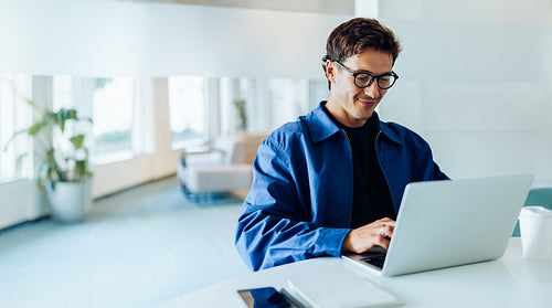 Man at laptop in blue jacket works in office