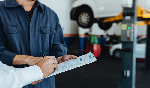 Auto mechanic taking sign on document from customer 
