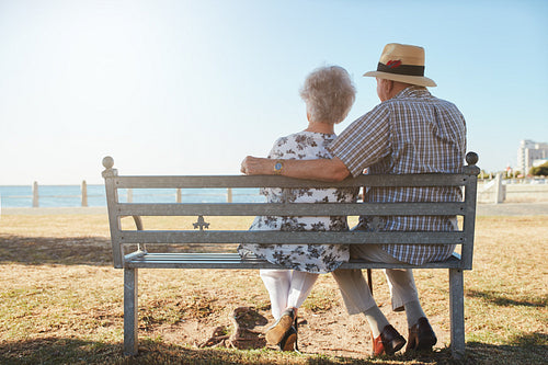 Elderly couple relaxing on a bench looking out to sea