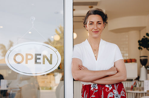 Mature small business owner standing at the entrance of her newly opened cafe
