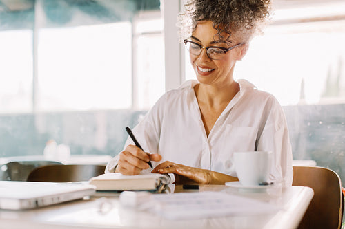 Happy businesswoman making notes in her journal