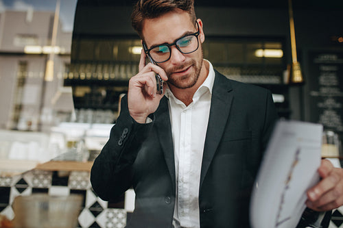 Entrepreneur talking on cell phone looking at office papers in a cafe
