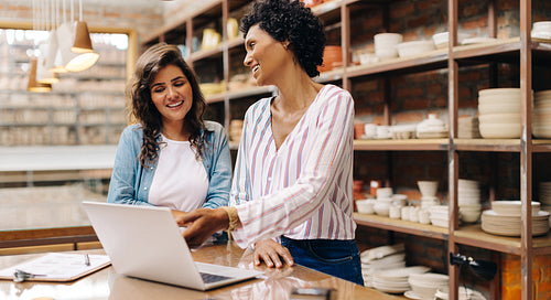 Smiling ceramists using a laptop together in their shop