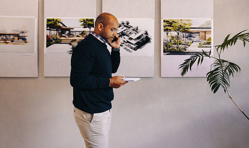 Architect talking on the phone while examining architectural drawings in an office