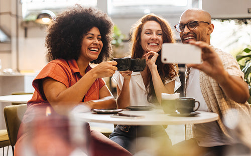 Group of happy friends taking selfies and making memories over coffee