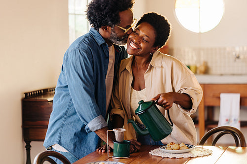 Afro couple sharing a kiss over coffee in their kitchen