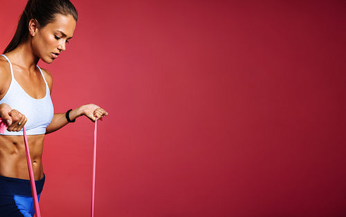 Fit woman doing strength training using resistance bands on maroon background