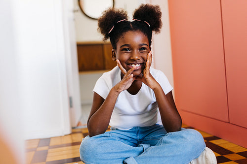 Happy young girl with afro hair smiling and sitting on floor at home