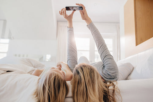 Mother and daughter lying on bed and taking selfie