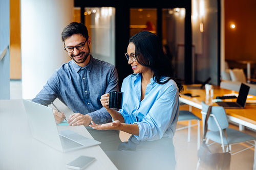 Two professionals discussing ideas over a laptop in an office setting