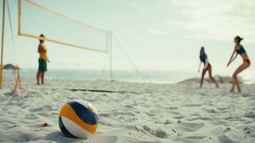 Static wide shot of a professional beach volleyball match with ball in the foreground