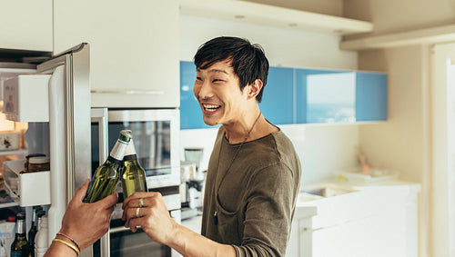 Asian man toasting a bottle of beer with friend