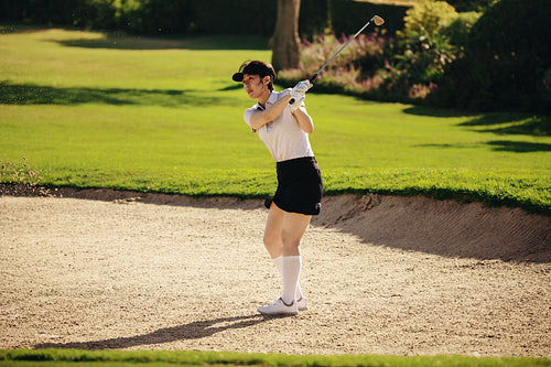 Action shot of sportswoman from a sand bunker on an immaculate golf course