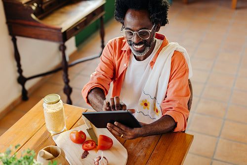 Cheerful man making traditional Brazilian cuisine at home using a digital tablet