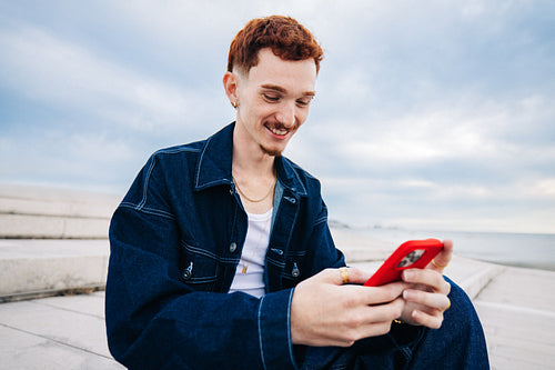 Young man smiling while using phone by the sea