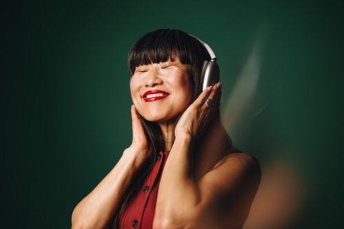 With eyes closed, the woman enjoys headphones in a close up studio portrait