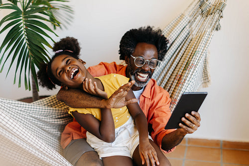 Father and daughter laughing and engaging in a video call with a tablet